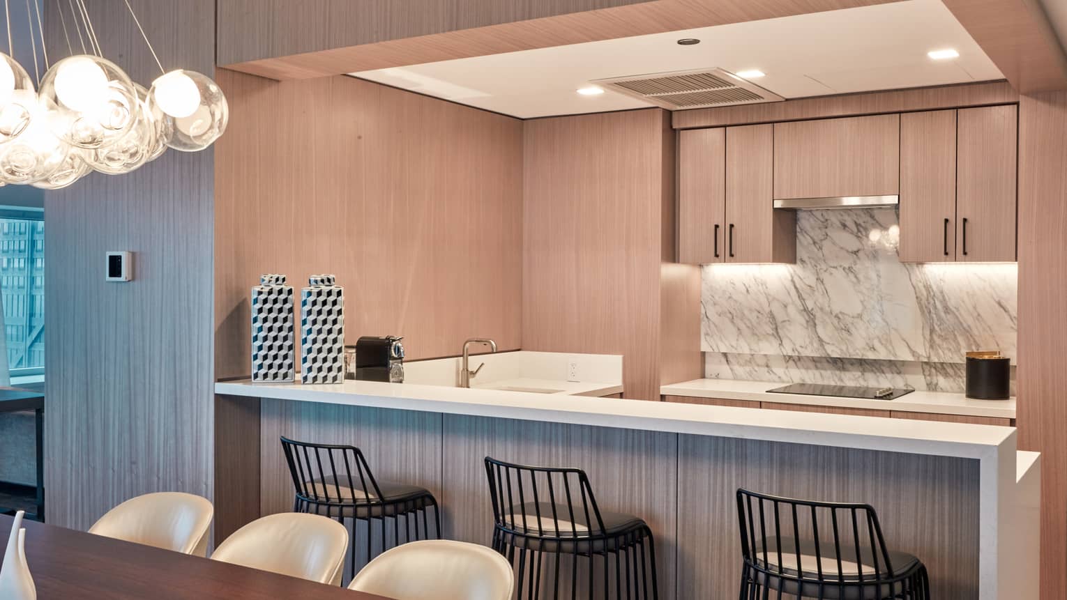 Kitchen with light wood cabinets, marble backsplash, three metal counter-height chairs