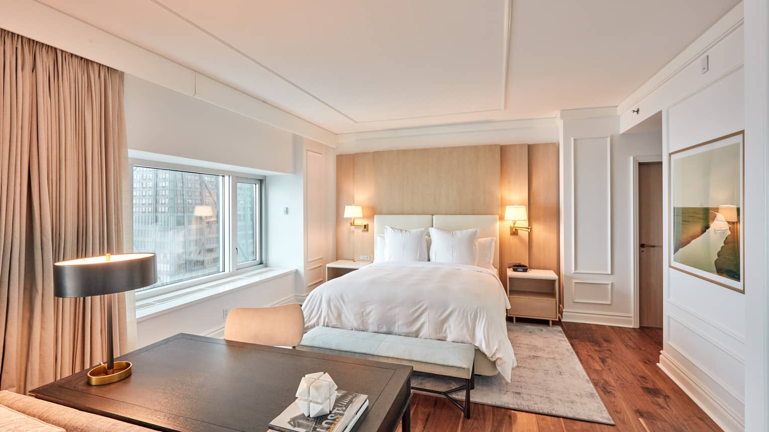 Bedroom with queen bed, dark wooden desk, rich wood floors, white walls, window