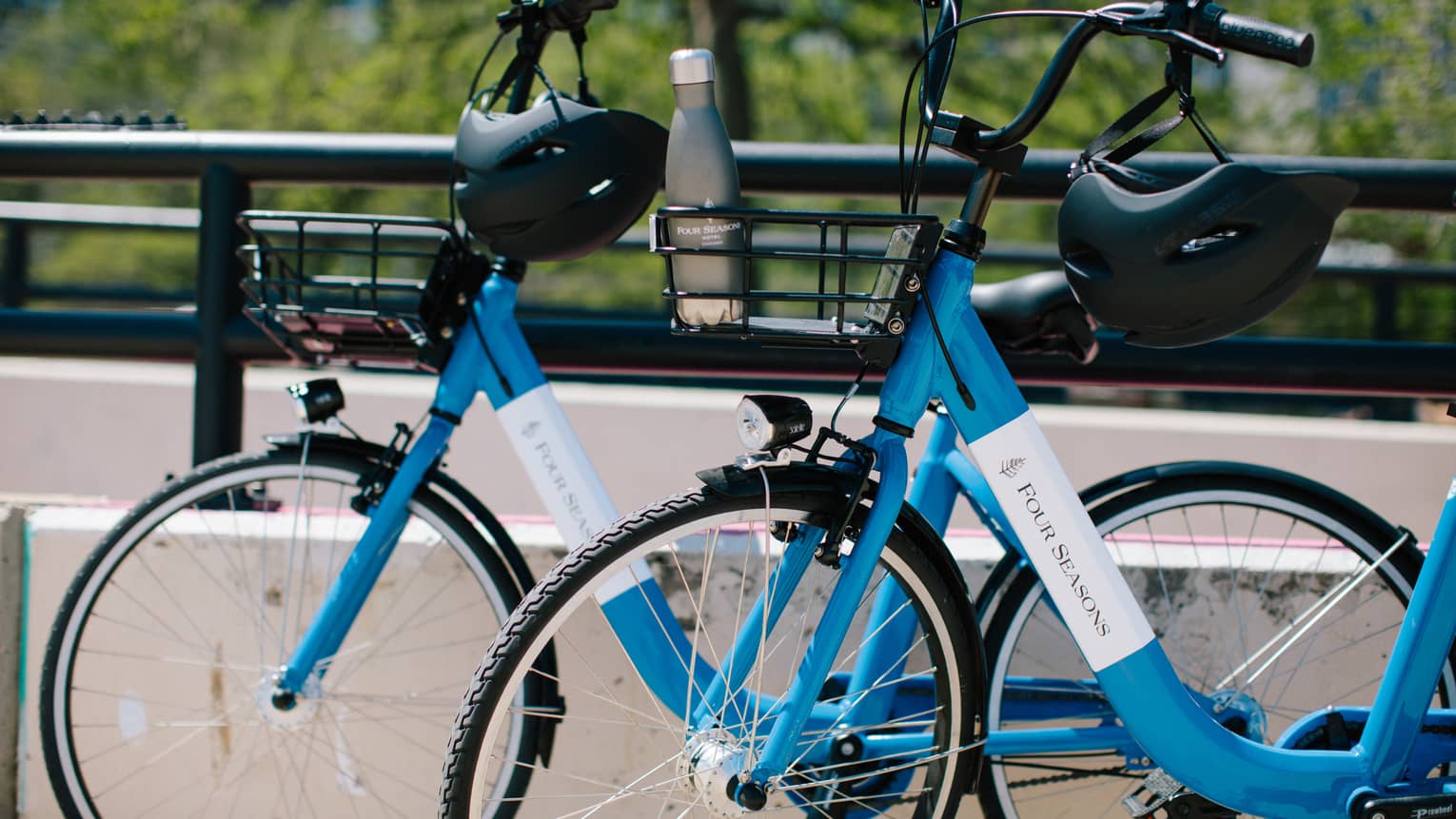 Close-up of two blue Four Seasons bicycles with helmets hanging on the handlebars and a water bottle in one bicycle's basket.