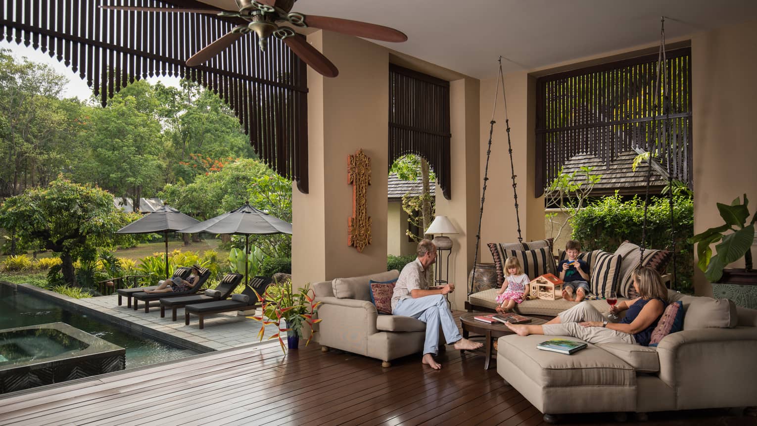 A family sits on an L-shaped couch overlooking a private pool and cabana. 