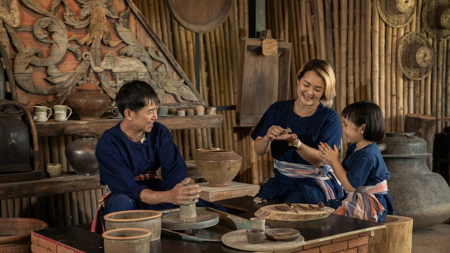 A potter teaching a woman and a child to shape clay in a rustic pottery workshop, surrounded by traditional tools and pottery.