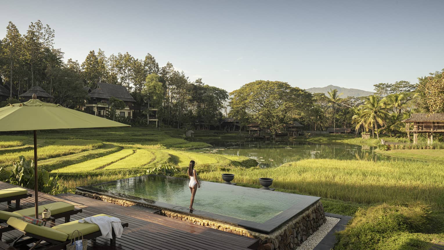 Woman in white bathing suit stands in front of pool overlooking rice paddies