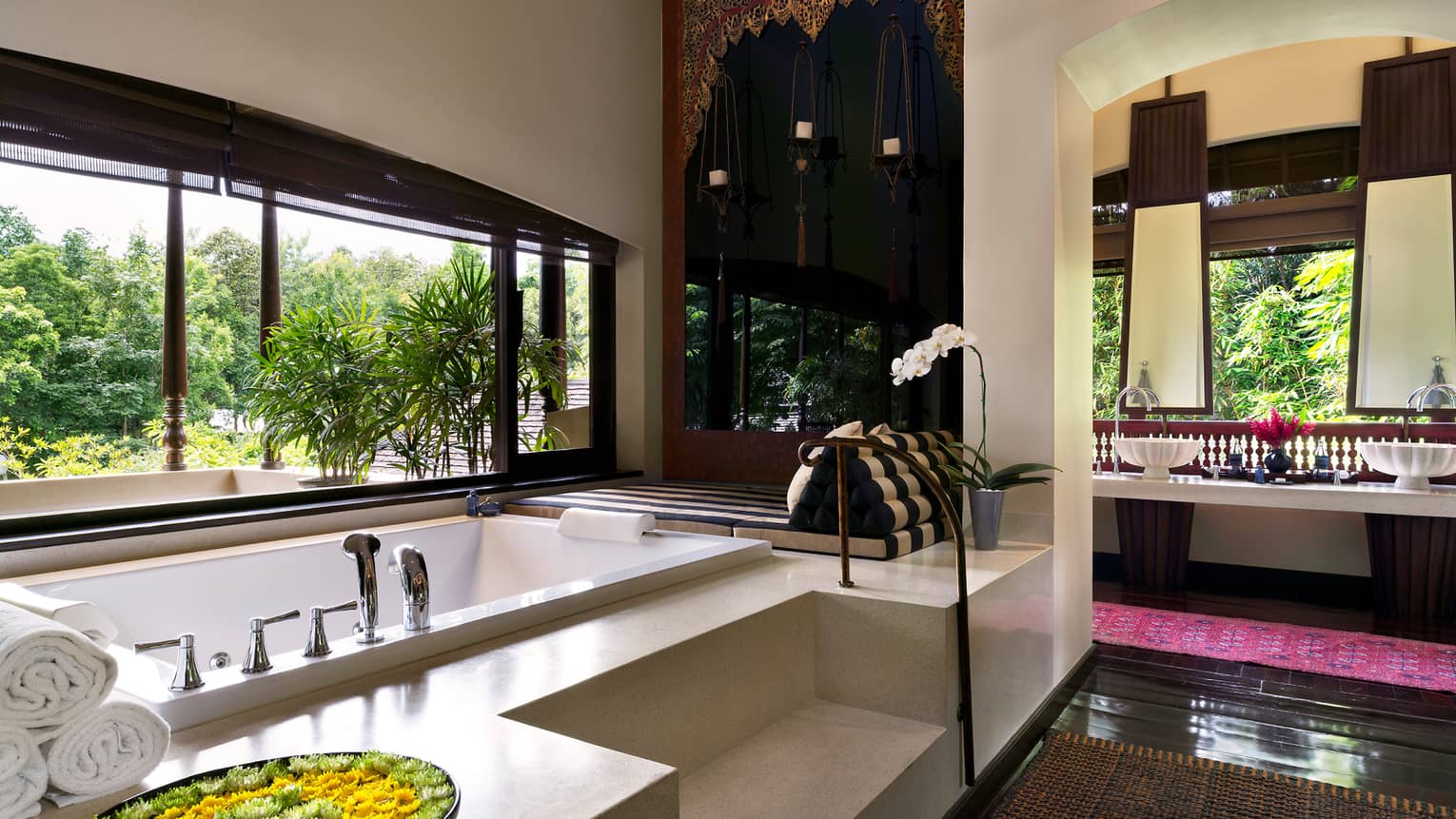 Luxurious bathroom with a sunken bathtub daybed and double vanity surrounded by large windows and tropical views