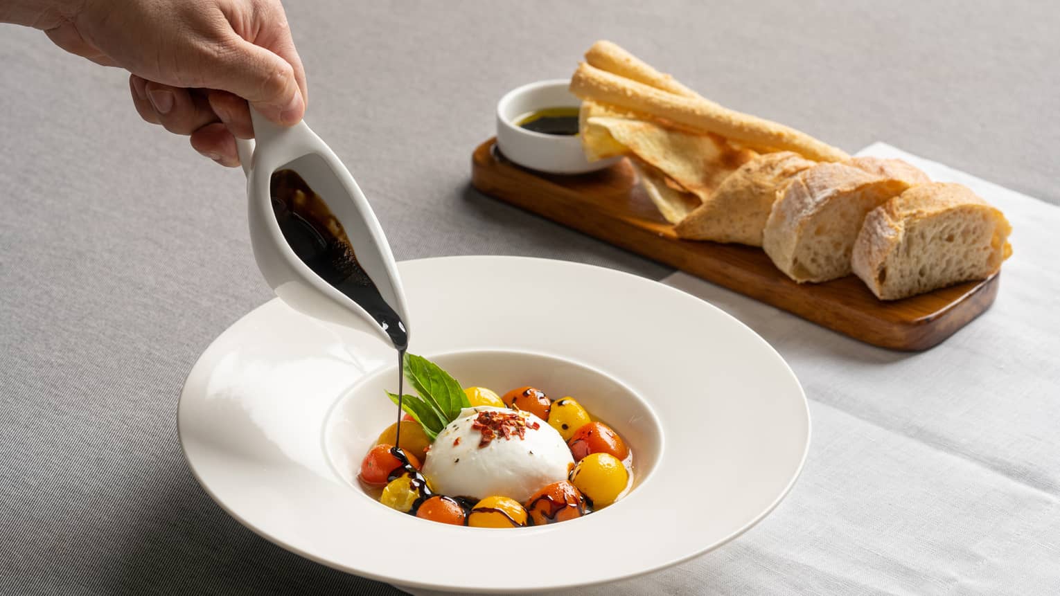 Burrata encircled with red and yellow cherry tomatoes in a white, large-rimmed bowl