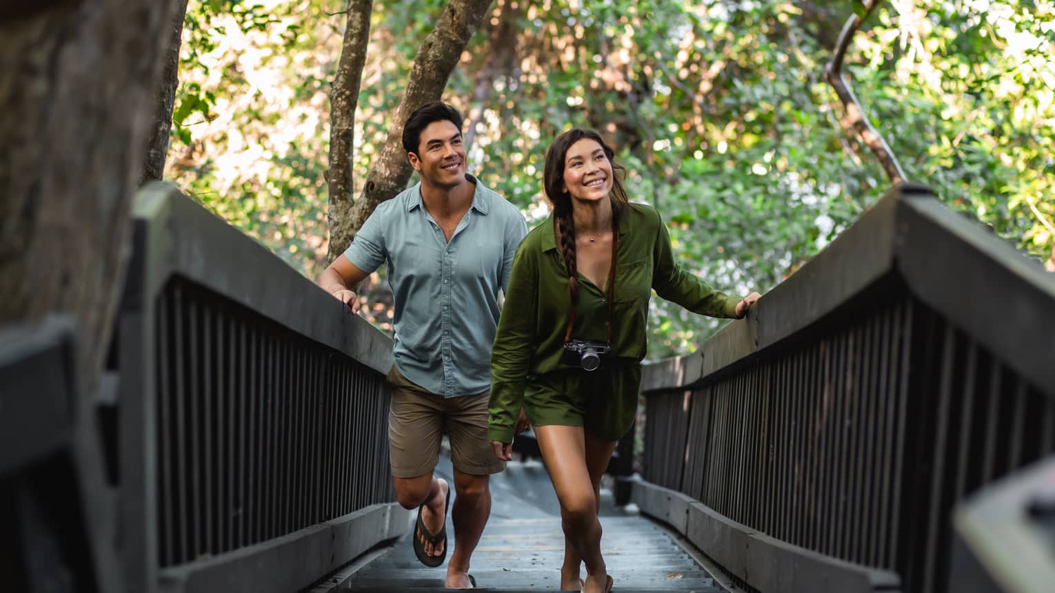 A man and a woman walk up a wooden walkway surrounded by trees