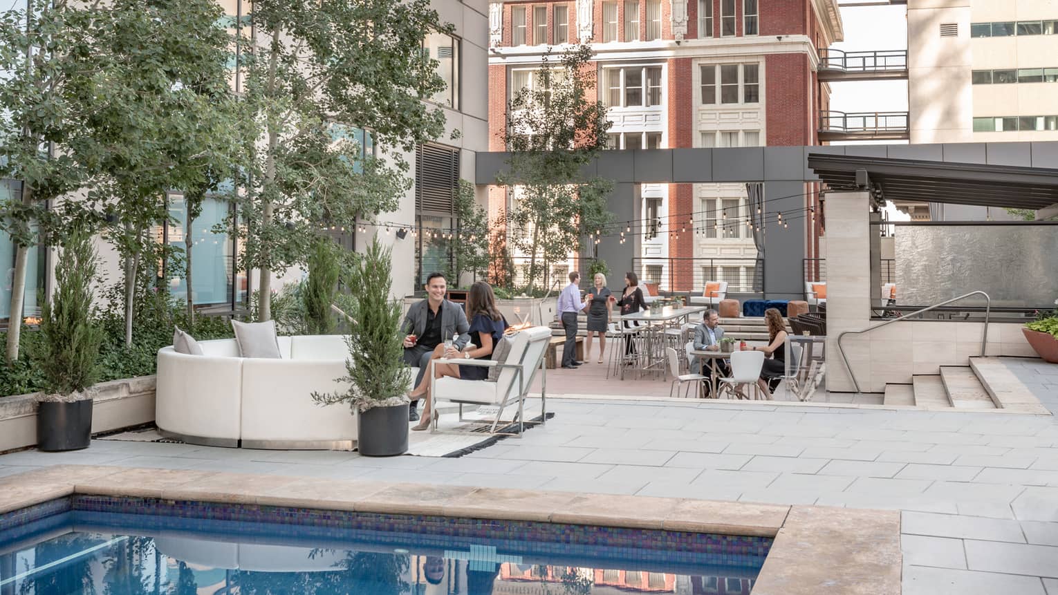 Couples, friends wearing business attire enjoy cocktails on outdoor patio lounge by swimming pool