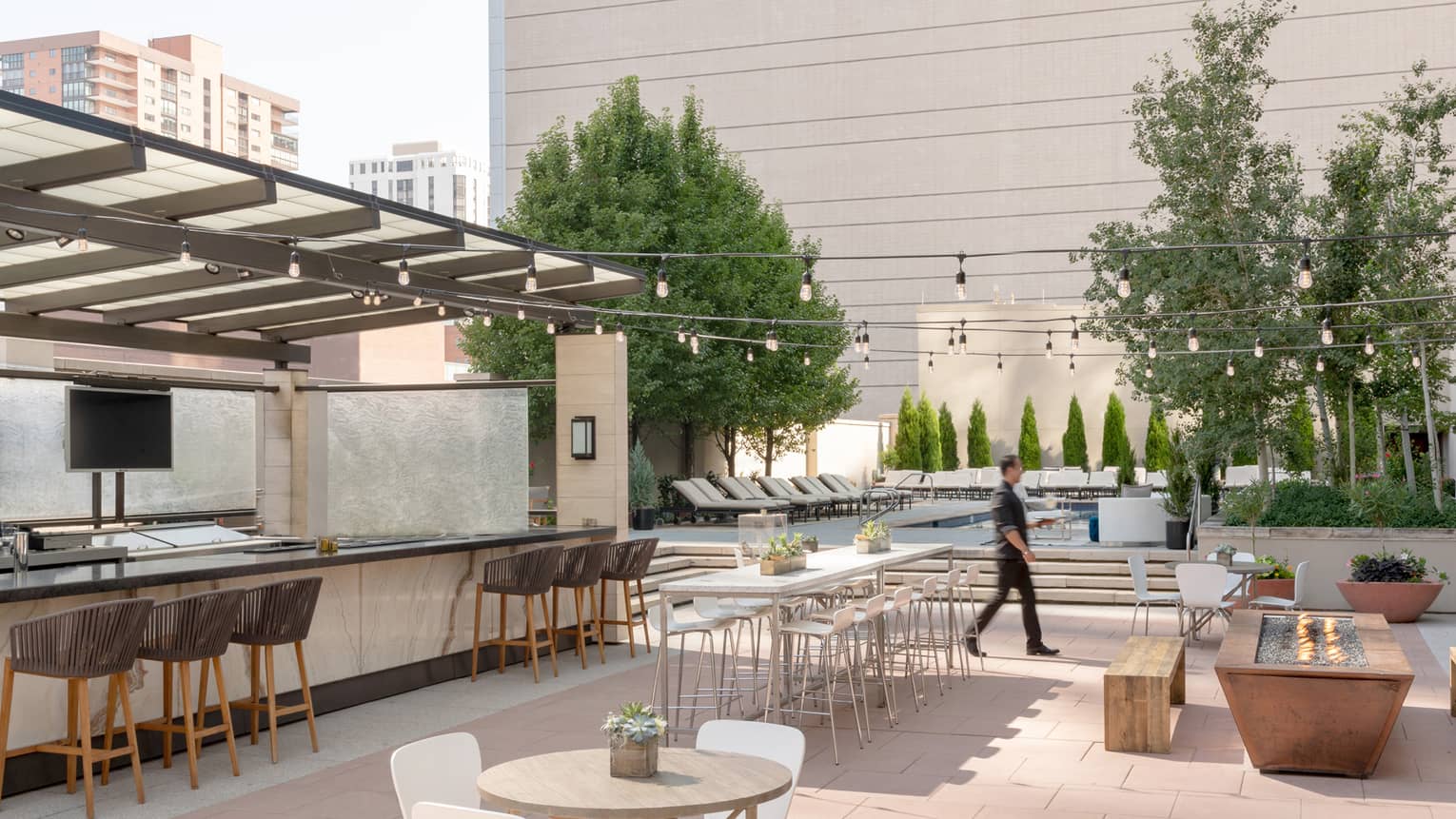 Man walks across sunny outdoor patio bar by tables, benches 