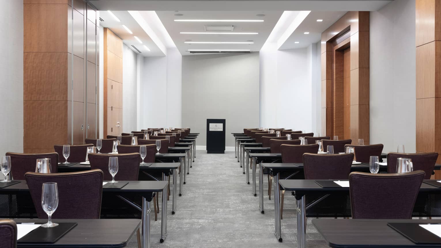 Rows of desks and chairs facing a podium on the other side of a long room.