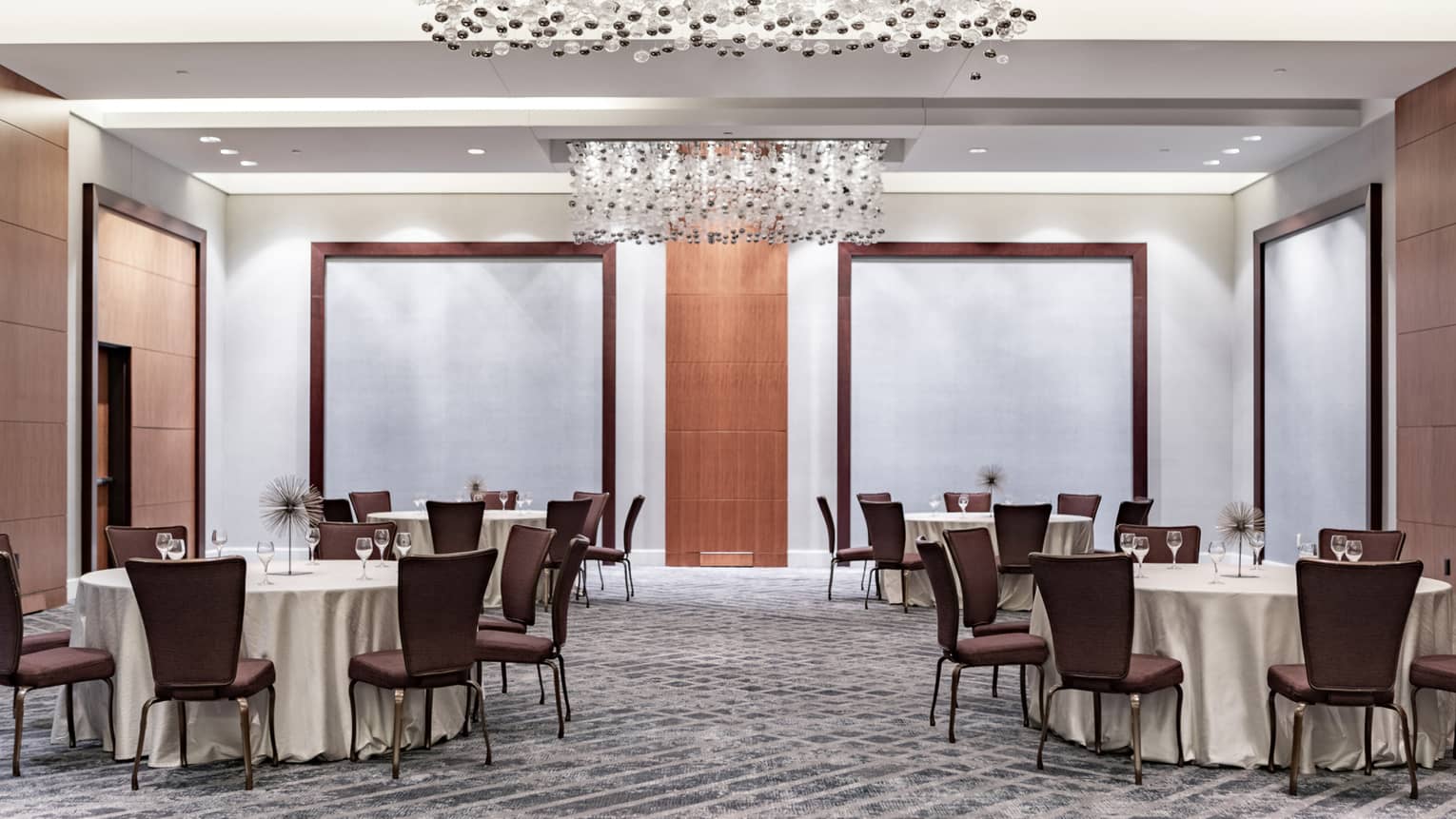 A well lit meeting room with four large round tables and brown chairs.