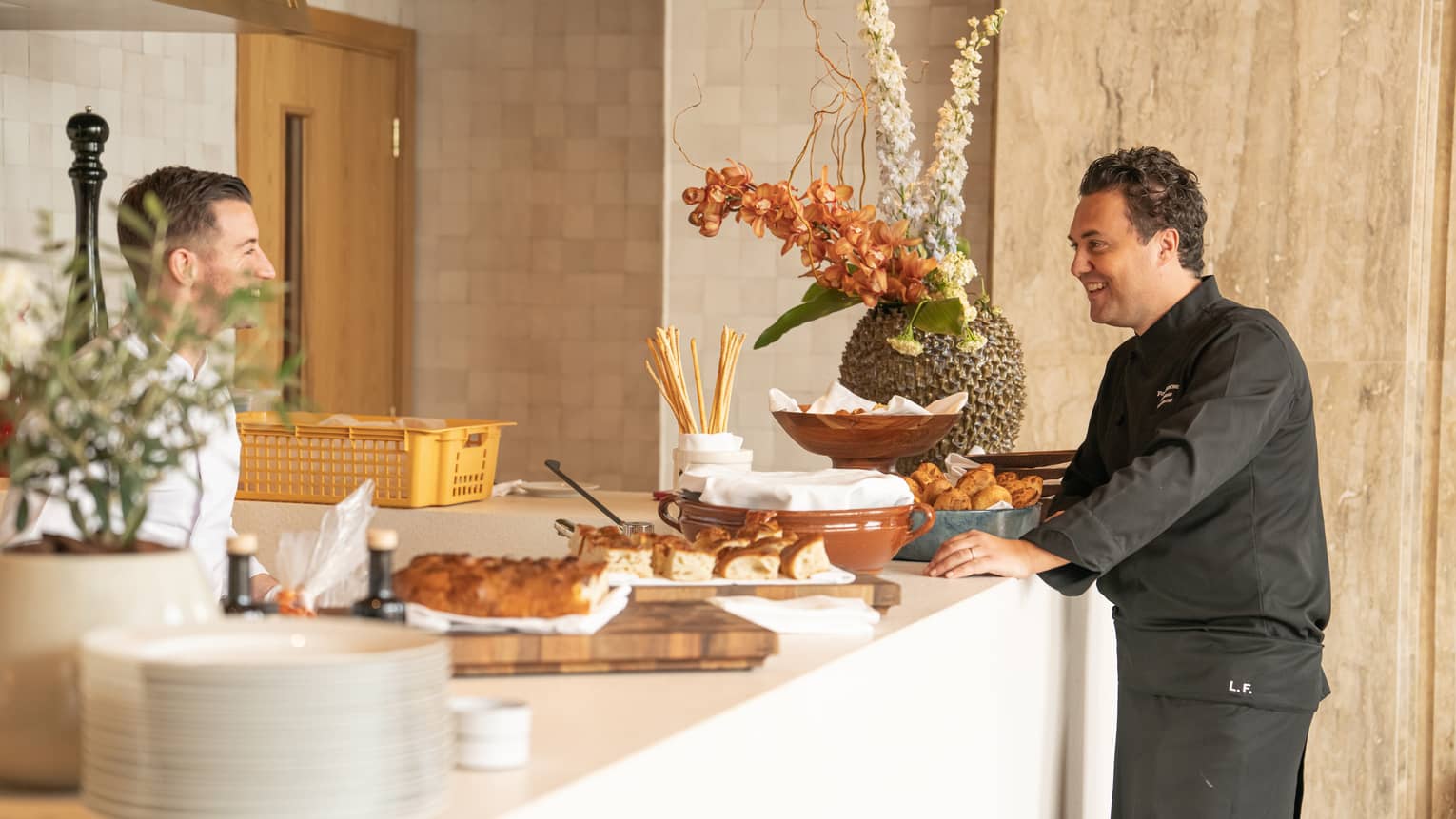 Two servers stand smiling at each other next to a counter filled with burnch buffet items