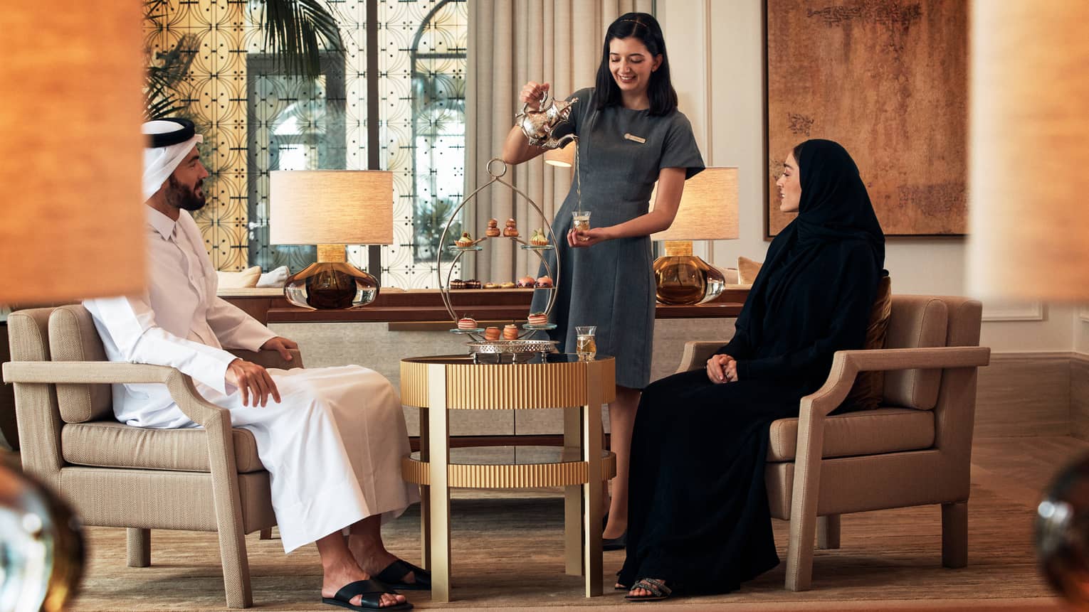 Woman serves afternoon tea to two people in luxury hotel lounge