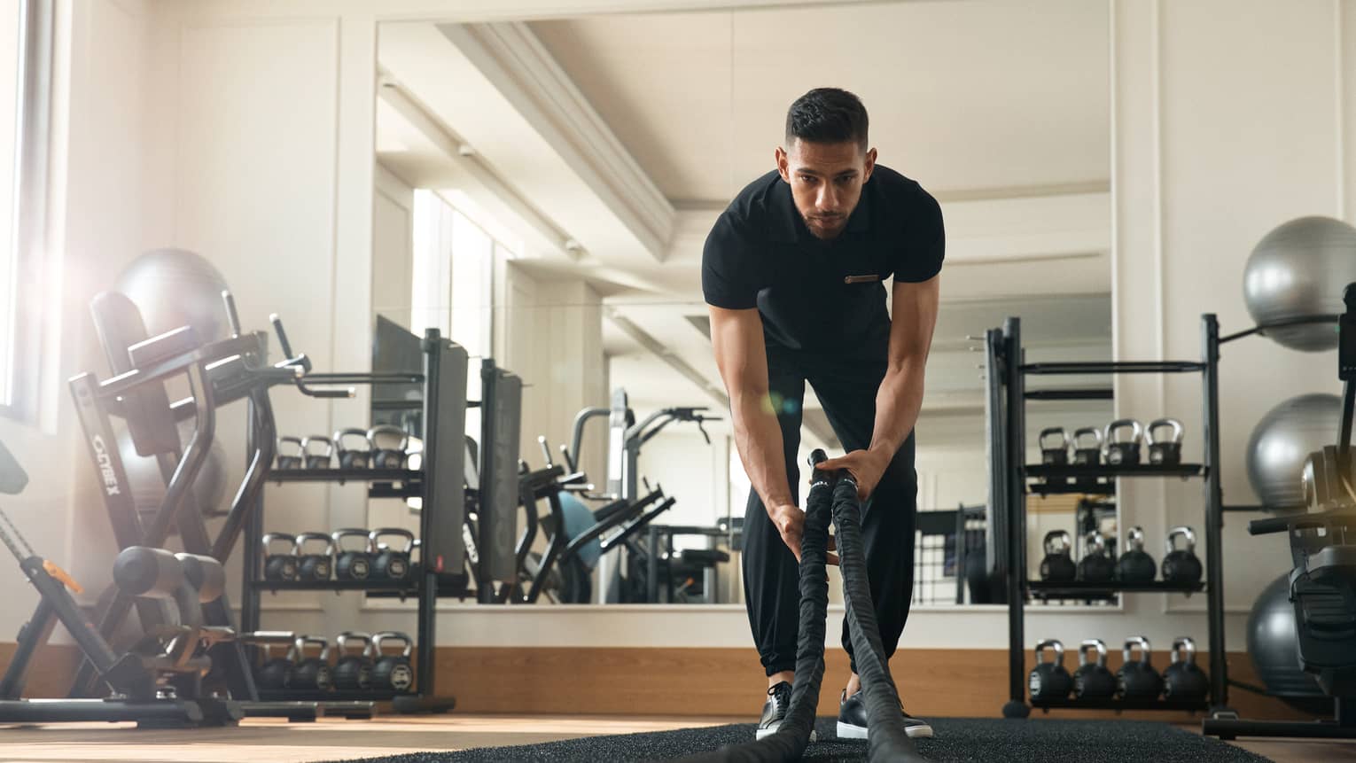 Man works out in fitness room using a heavy rope