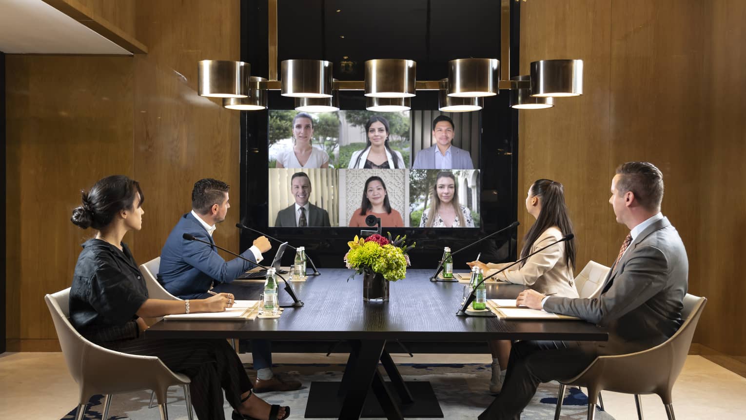 Hybrid meeting boardroom with in-person attendees and virtual attendees on video-conferencing screen
