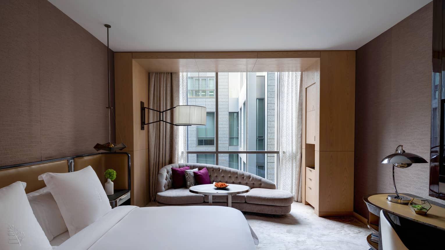 Bedroom with king bed, white sheets, brown walls and chaise by window