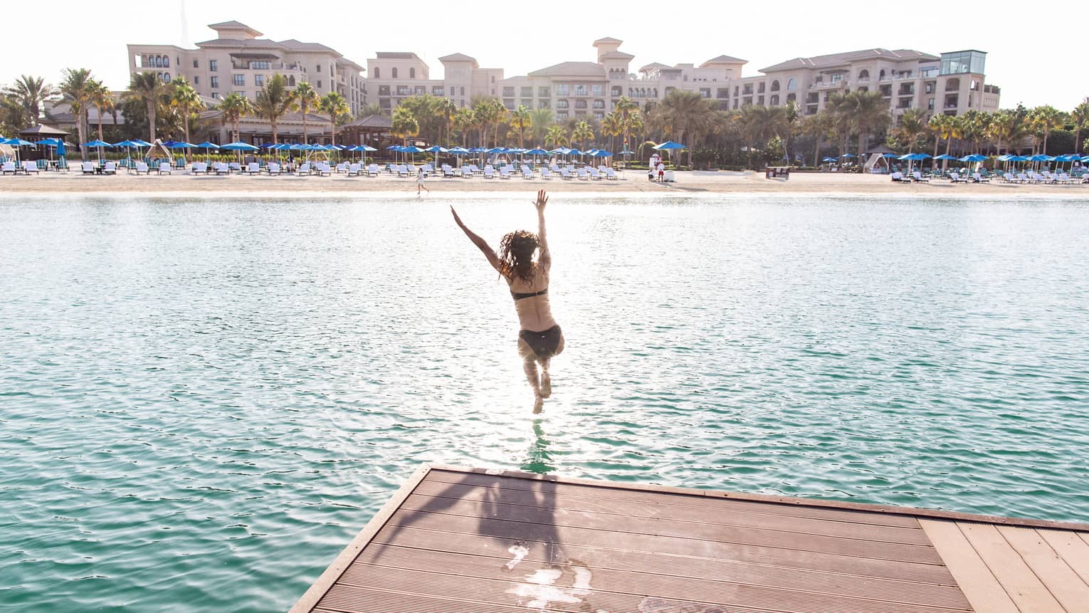 A woman jumps into a light blue lagoon.