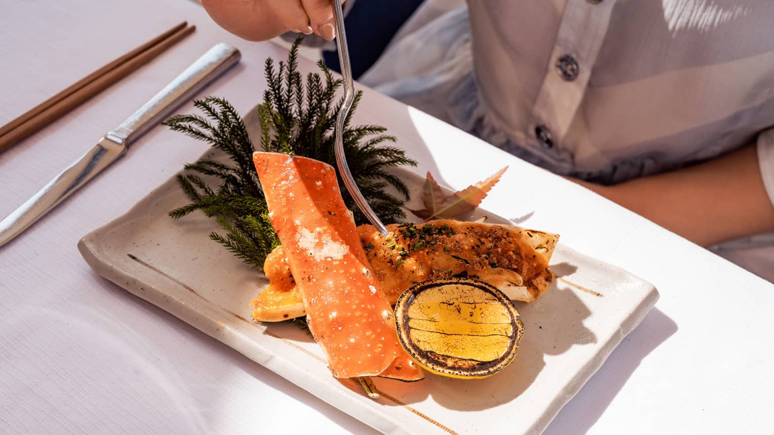 A man in a buttoned shirt eating a large cut of crab served on seaweed with a yellow sauce.