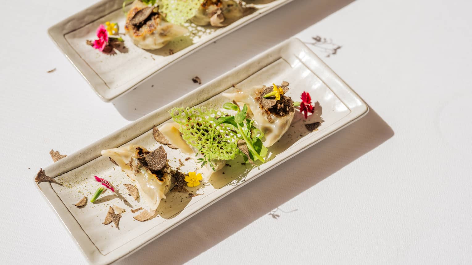 Two platters of gyoza with greenery served on a white table.