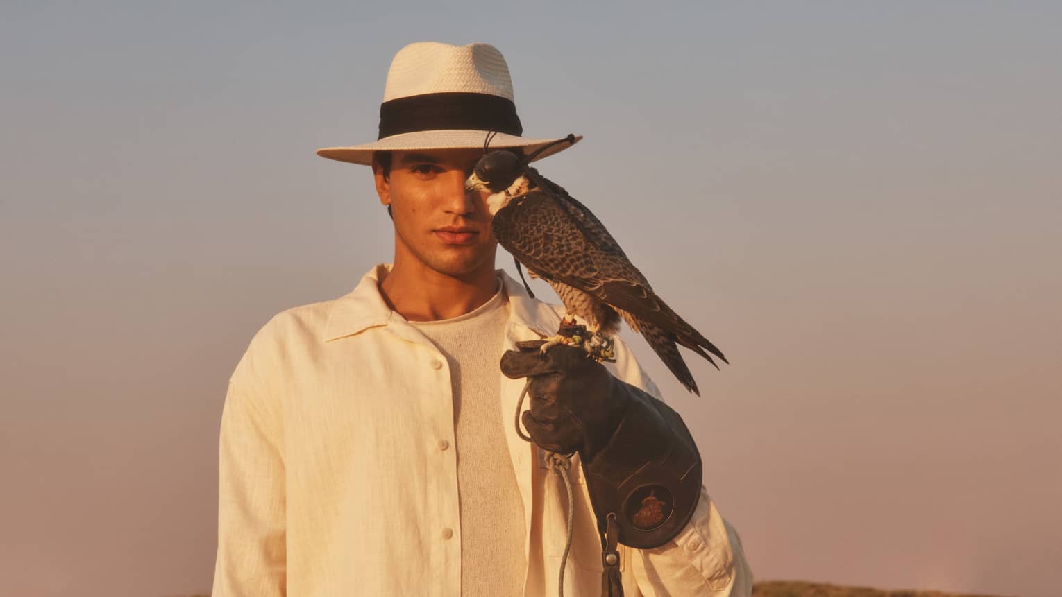 Person in straw hat and white shirt with gloved hand outstretched and hawk perched on it
