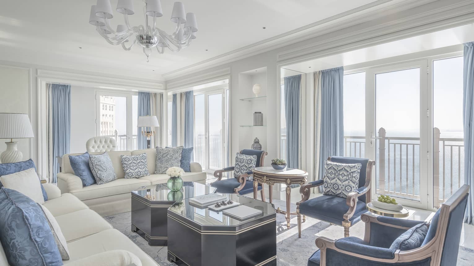 Living room with two white sofas, three blue arm chairs, blue curtains, two coffee tables