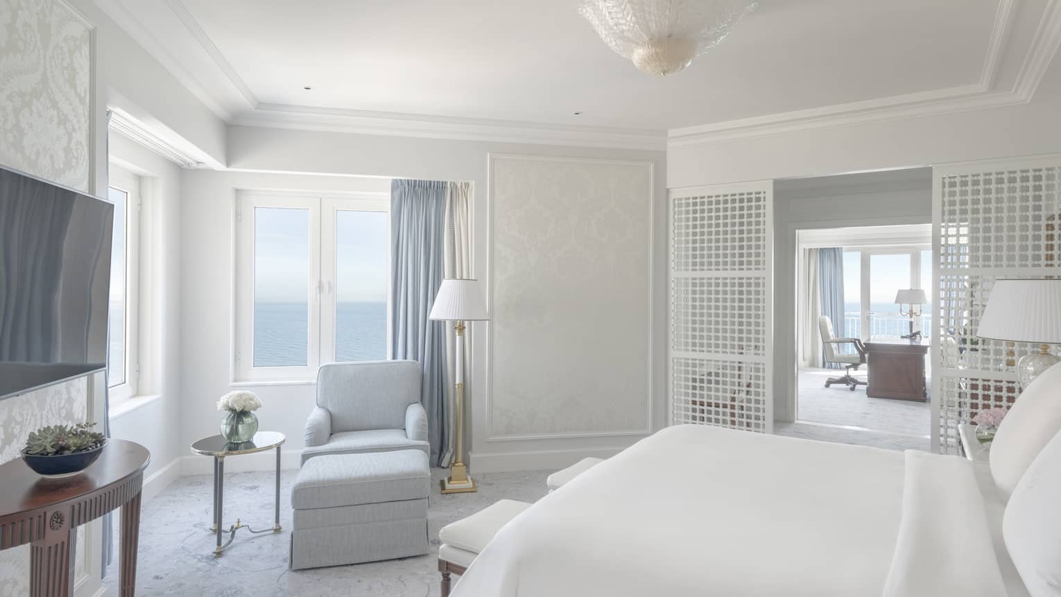 Sun-lit bedroom with king bed, white walls, light blue curtains and a light blue arm chair
