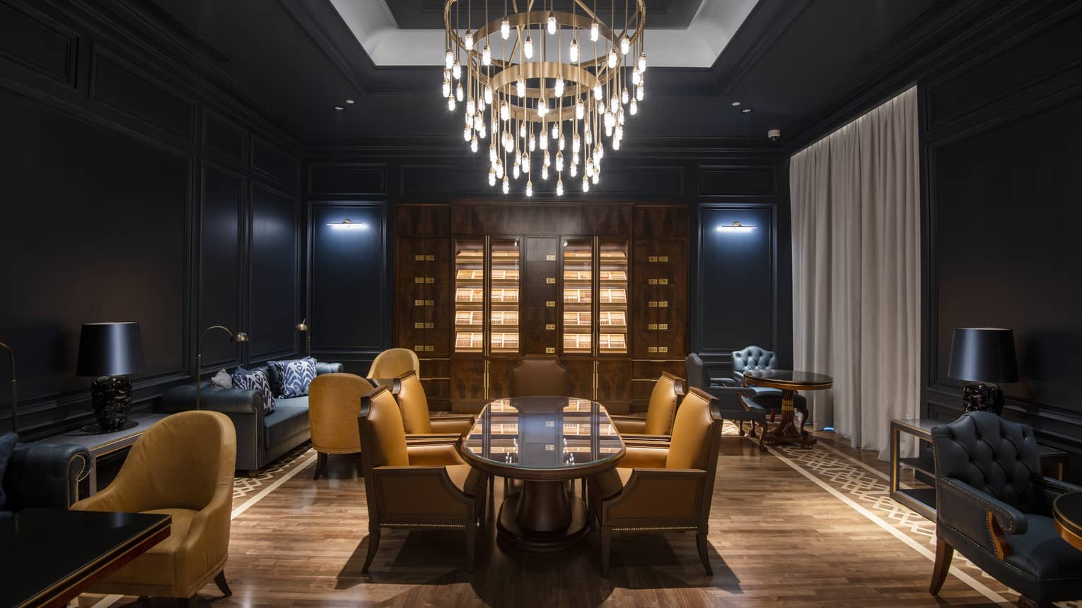 A dimly lit lounge area with tables, chairs and a chandelier.