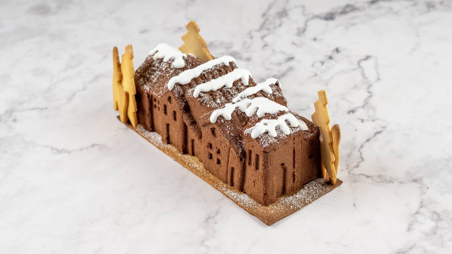 Yule log shaped to look like a small village with cookies as trees and white frosting on top