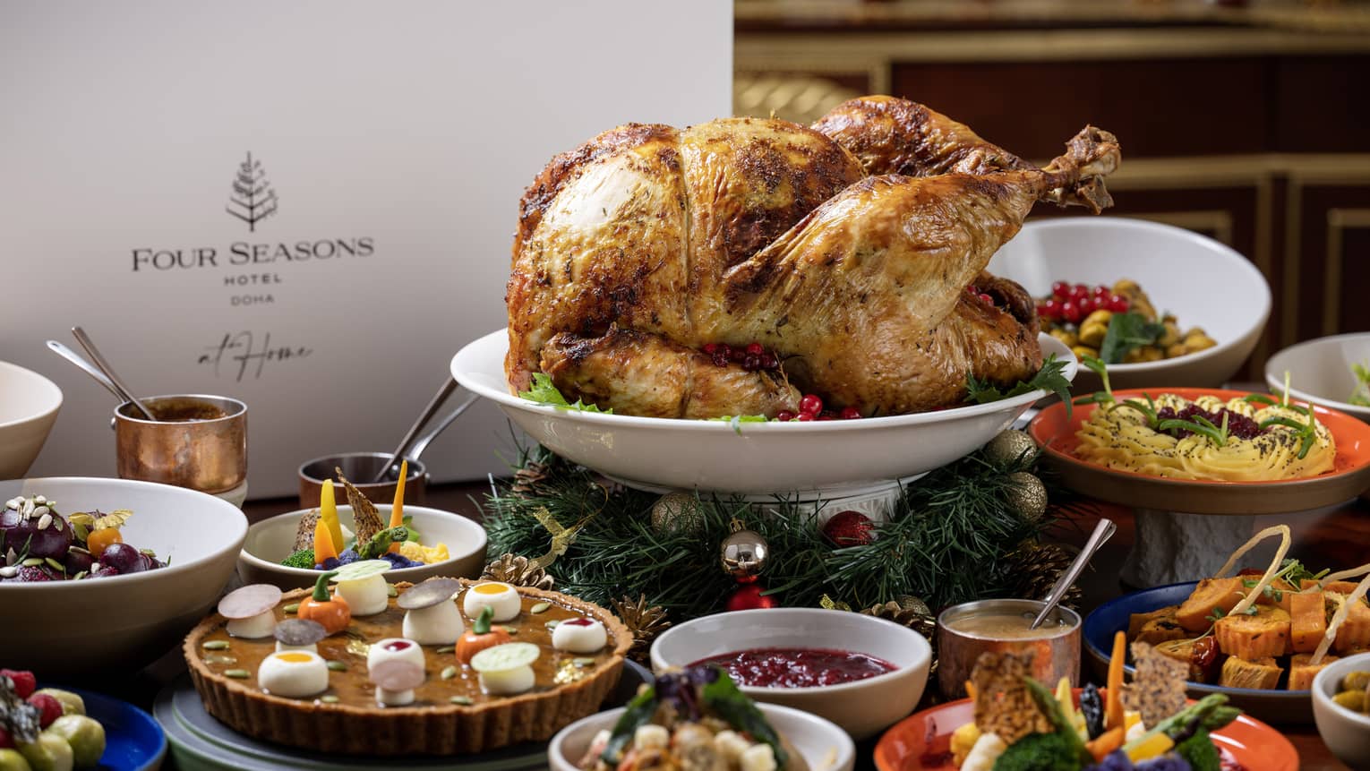 A whole roasted turkey on a white round platter sits elevated in the middle of a table filled with various bowls and plates of side dishes and sauces