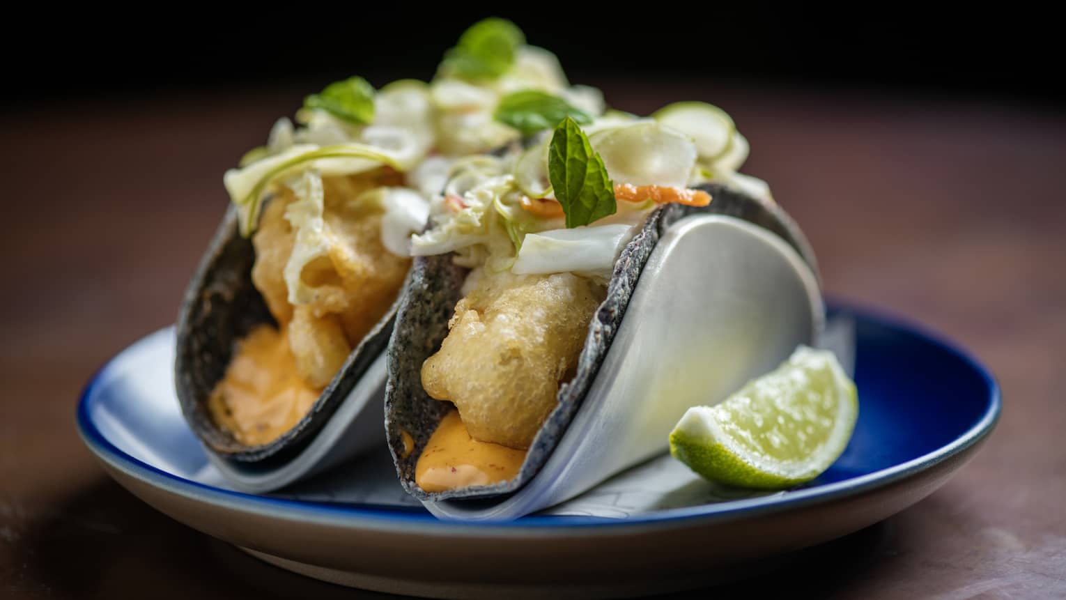 Two crispy fish tacos with aioli and cabbage-chili pickle served on a small blue plate