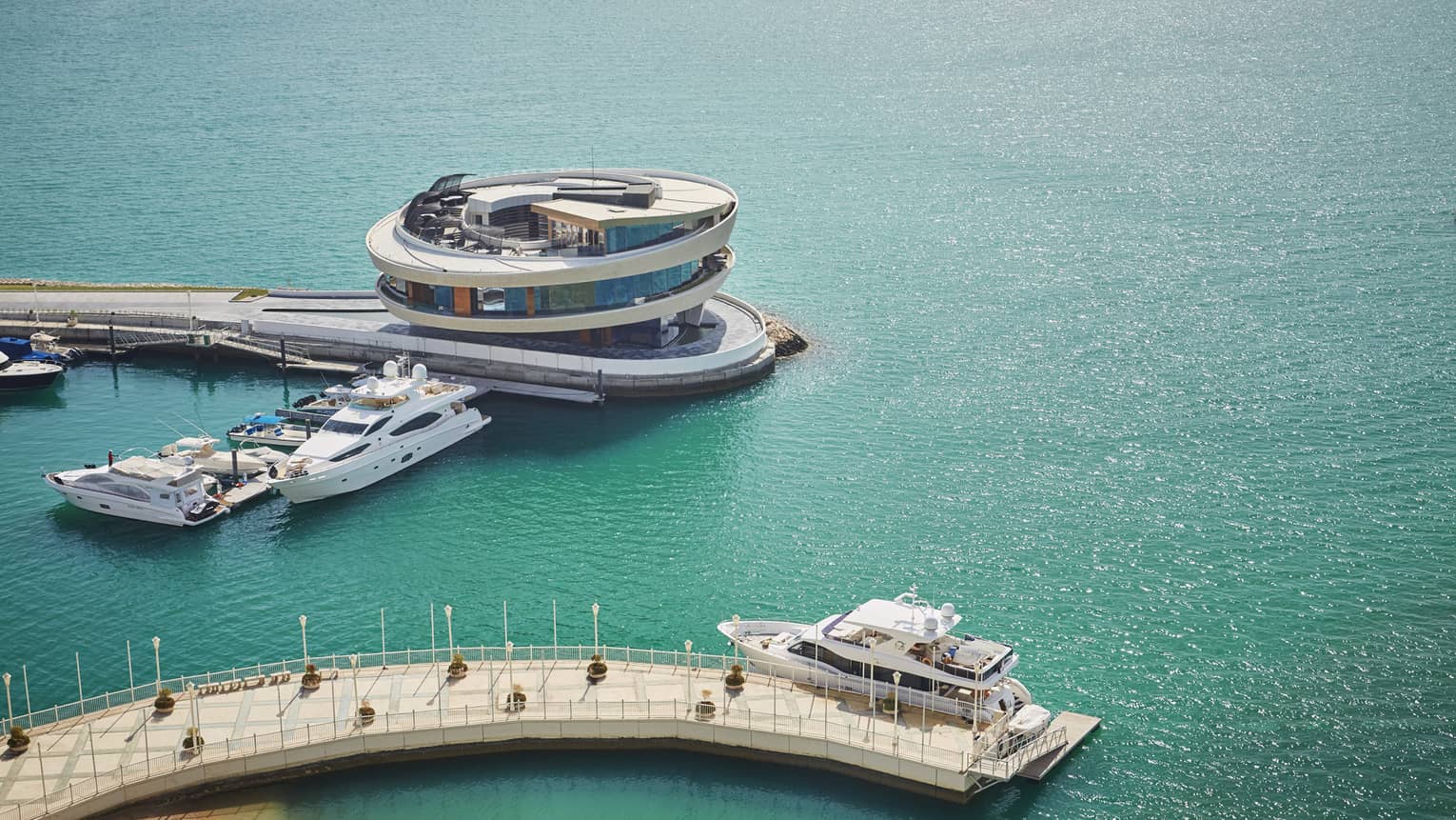 An aerial view turquoise waters and a yacht docking at a white, concrete dock in Doha 