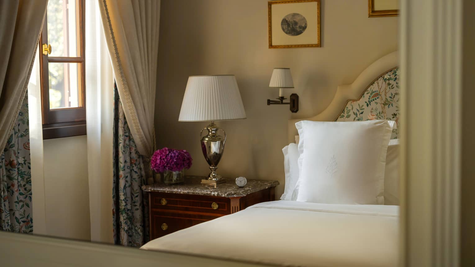 Hotel room bed, nightstand, lamp and a window with curtains