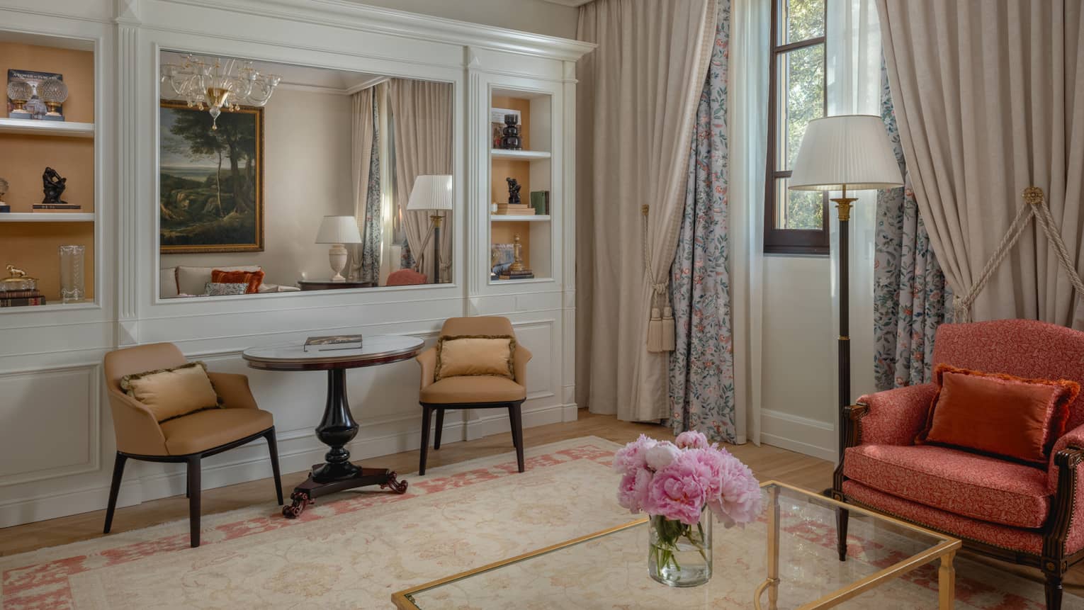 Hotel room featuring a living room, with built-in shelves, a table with two chairs, and a glass coffee table by a pink arm chair