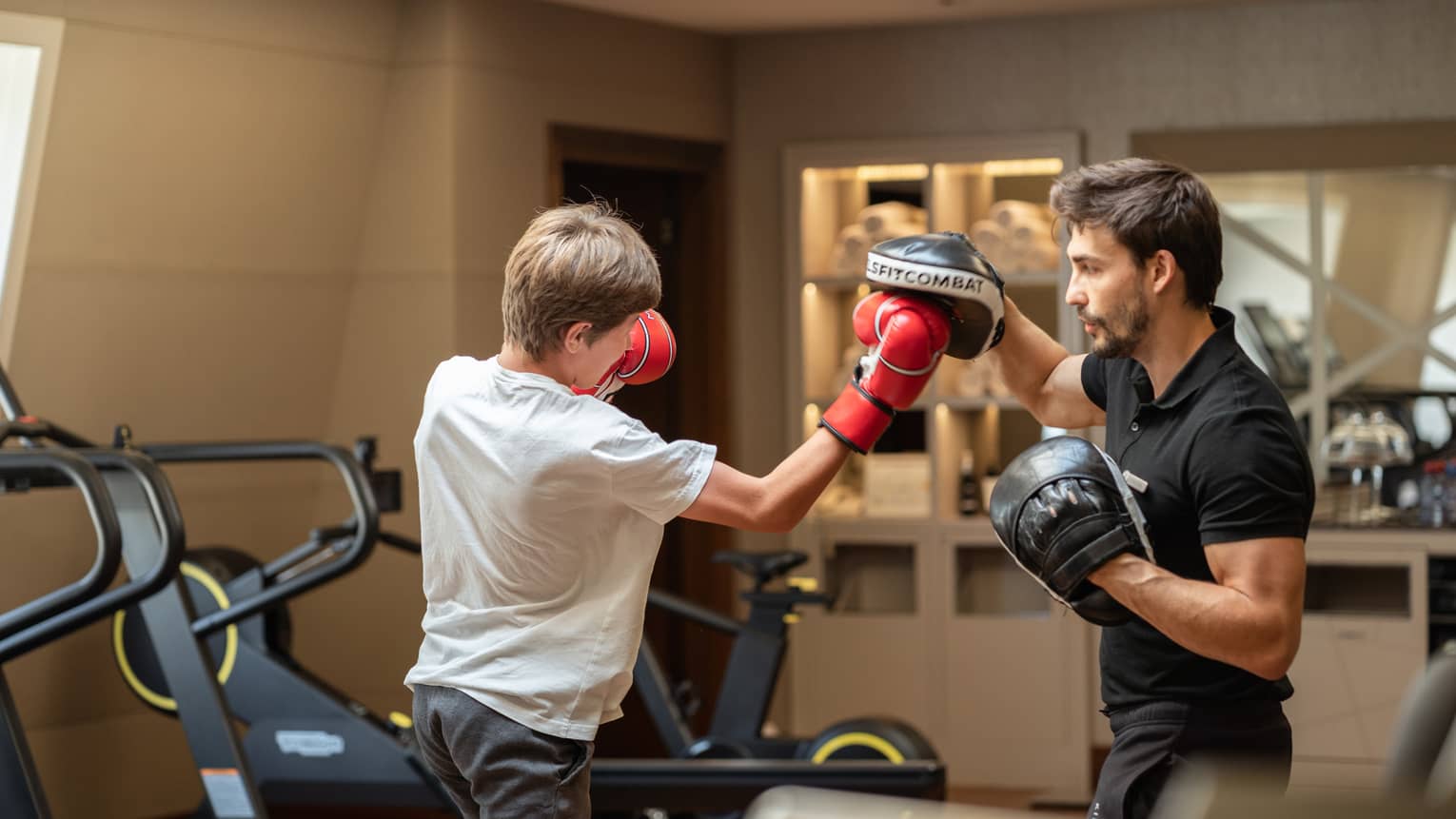 Teenager in red boxing gloves sparring with trainer in black boxing gloves in gym