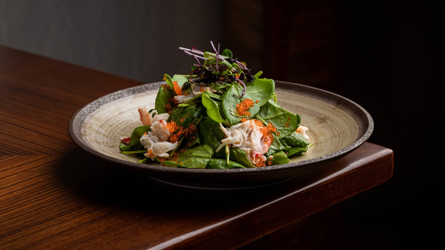 King Crab and Baby Spinach Salad on beige, round ceramic plate