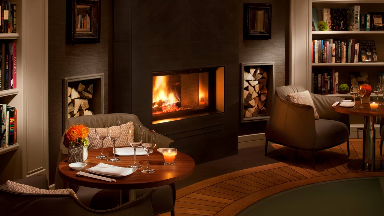 Candle-lit cocktail tables beside gas fireplace, bookshelves in dimly-lit lounge