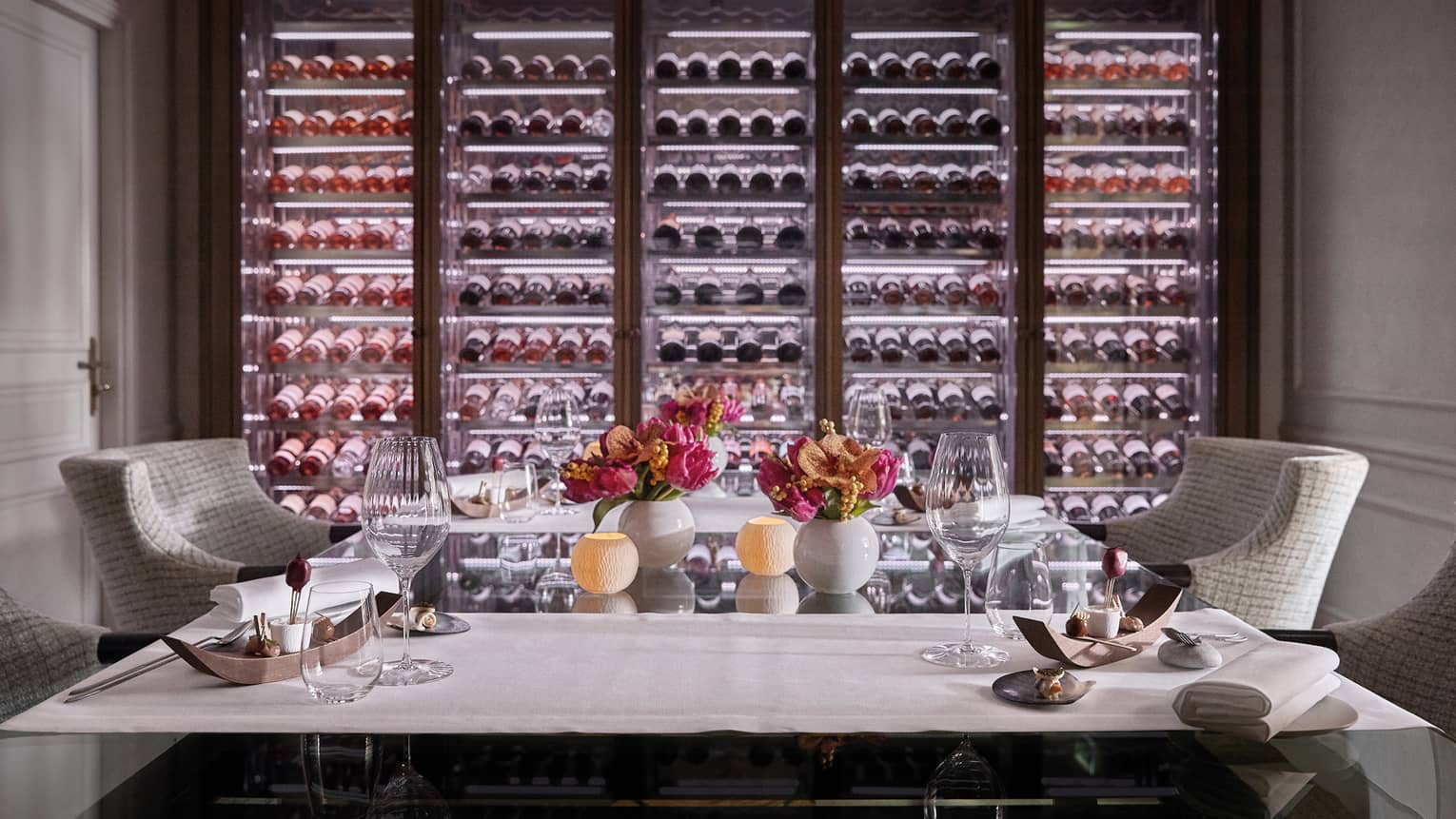 A private dining room with two chairs and an illuminated wall of wine on display