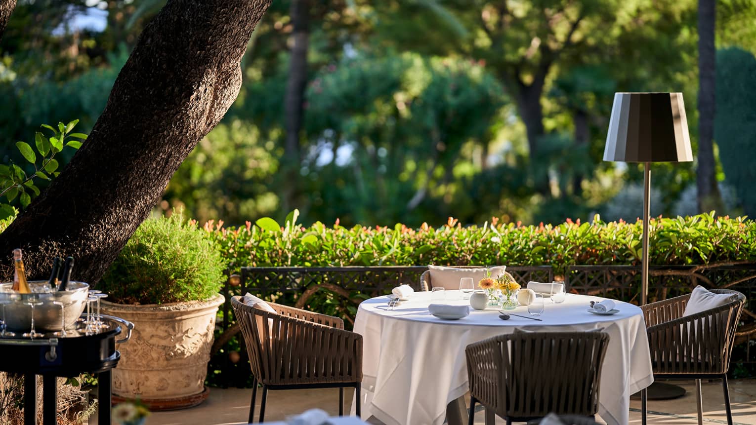 Le Cap restaurant terrace with Champagne stand, white round table, rattan chairs, hedge