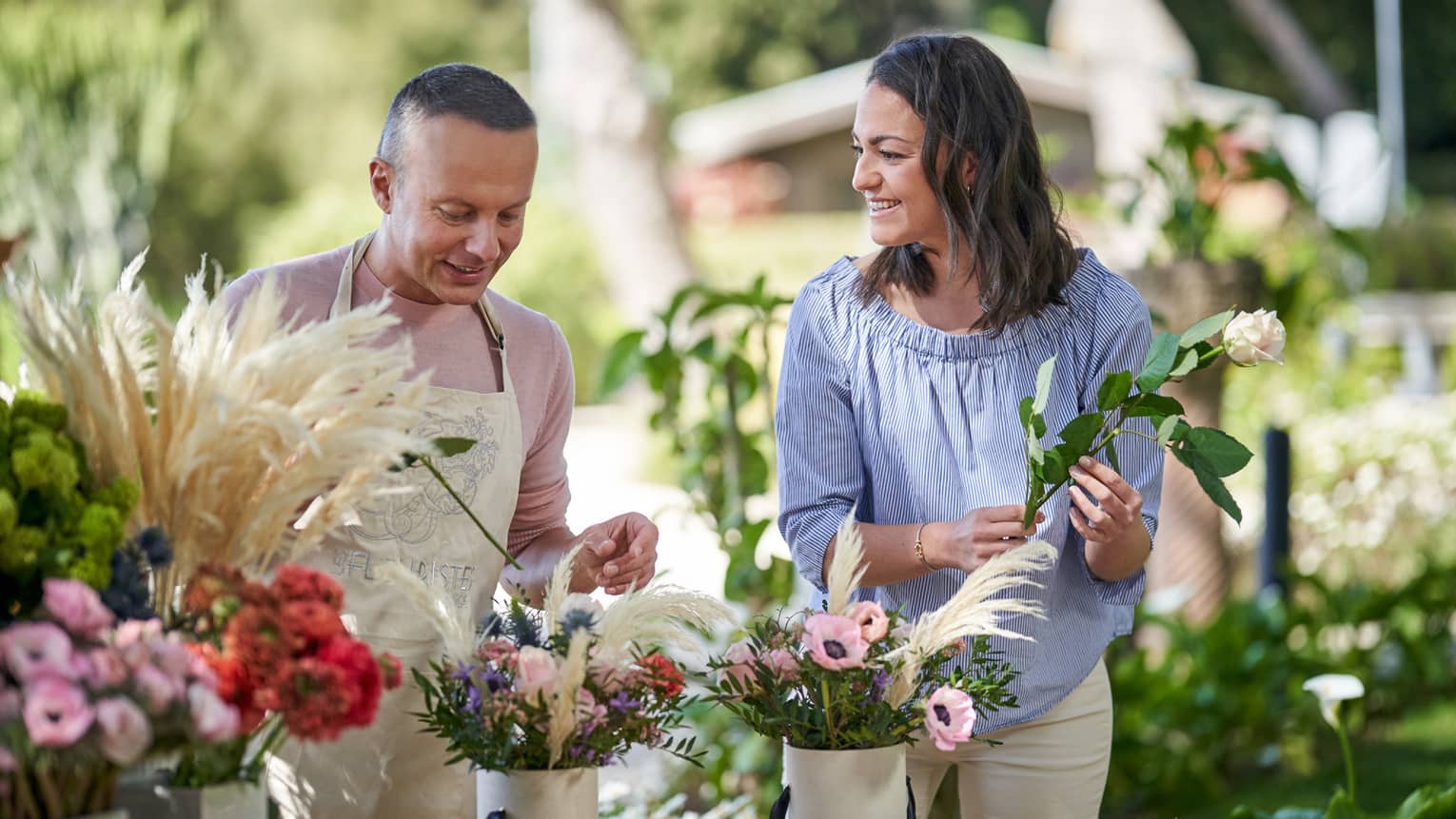 Two people stand outside at a table putting together floral bouquets