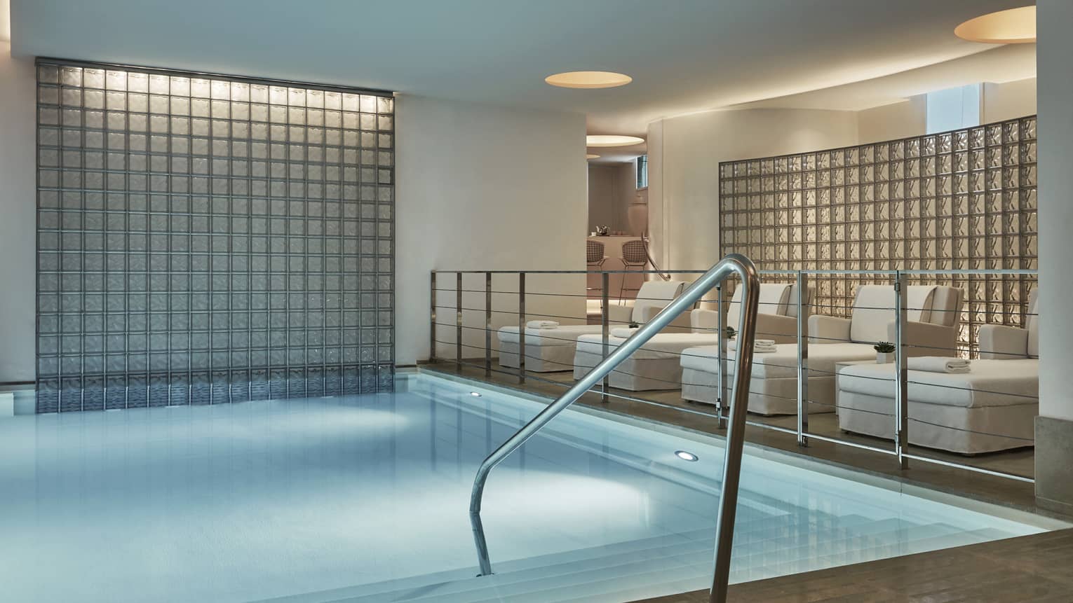 Railing into indoor spa pool under platform with white lounge chairs