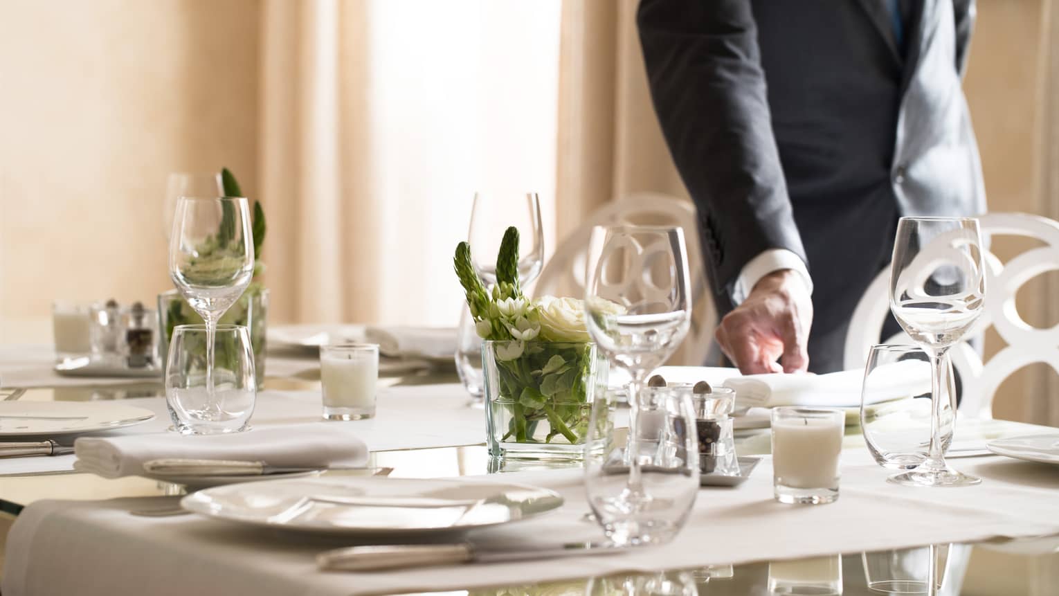 Hotel staff places napkin on small, elegant dining table in sunny room