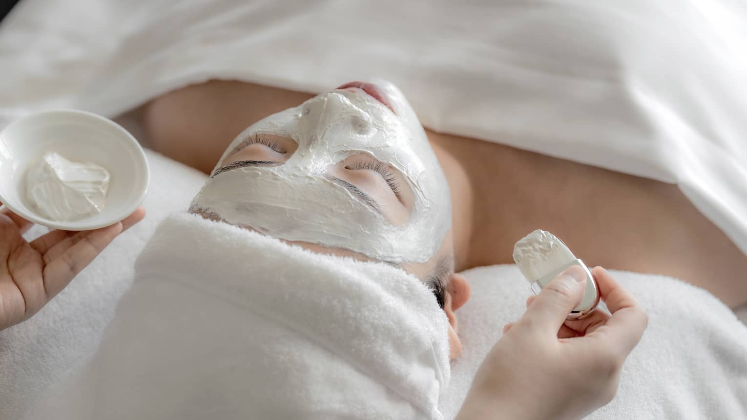 Spa therapist applies white clay mask to woman?s face at the Spa
