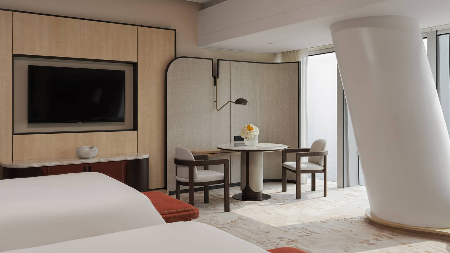 Contemporary hotel room with two beds, table and two chairs, TV and pillar
