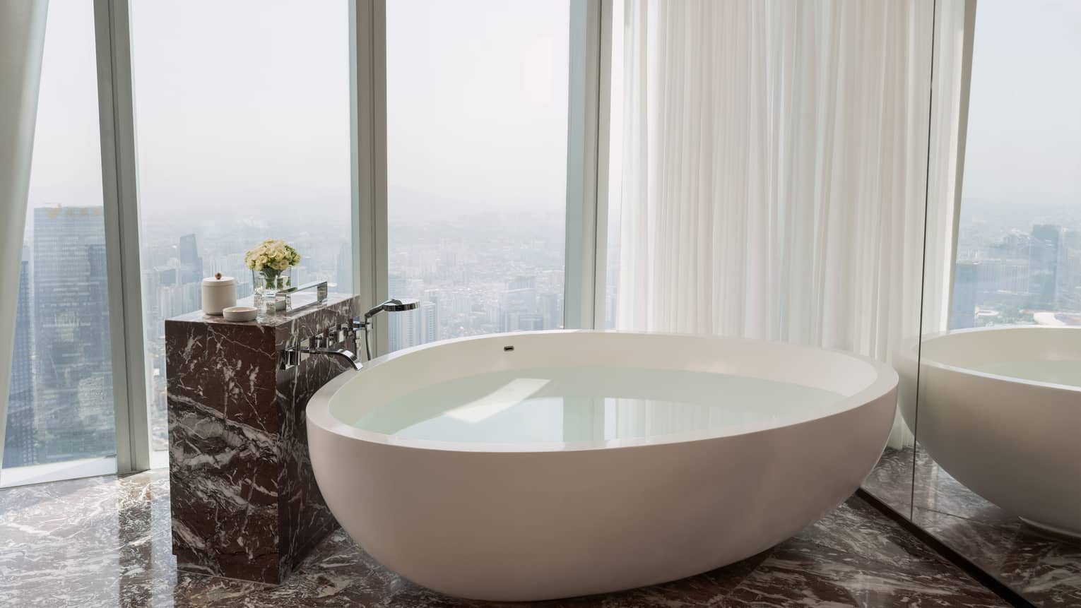 Bathroom with wall of windows overlooking city, and a large free-standing tub next to the windows