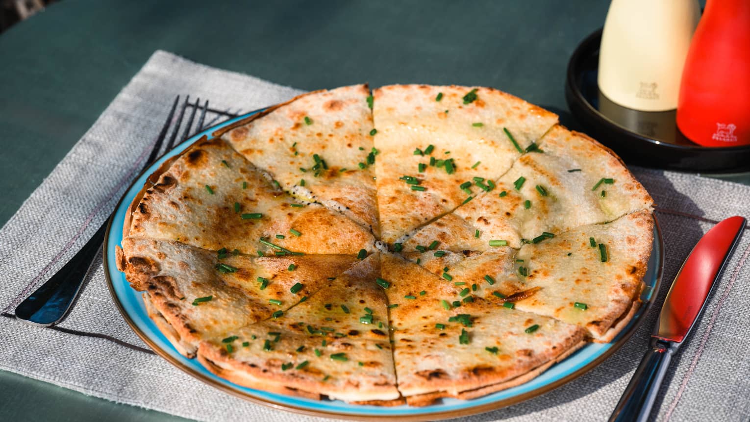 Focaccia round cut into triangles and dusted with chives on blue plate