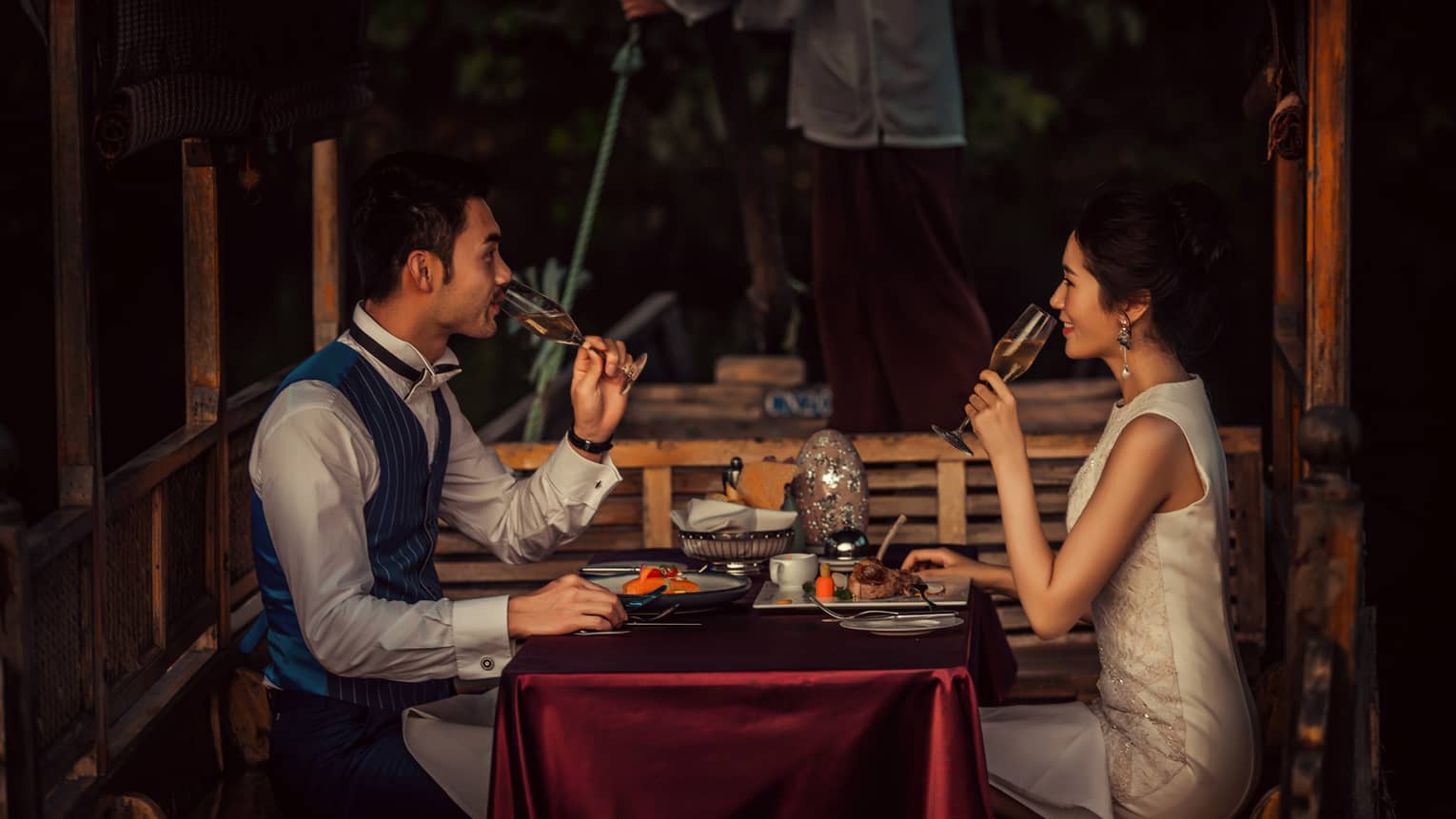 Couple sipping Champagne, dining at small table on traditional Chinese wooden boat