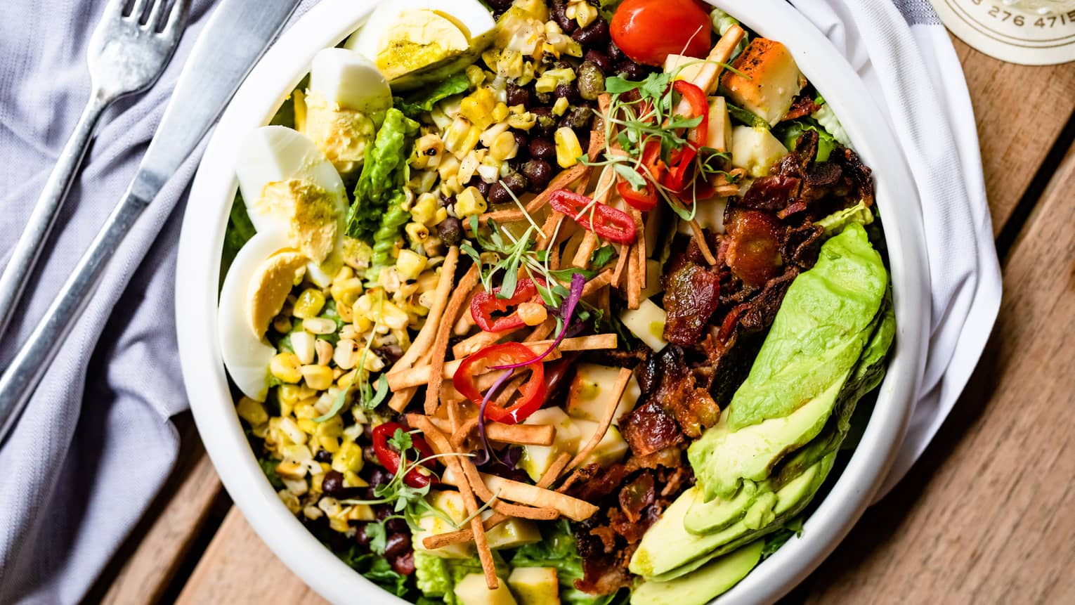 A large salad with corn, avocado, eggs, and more.