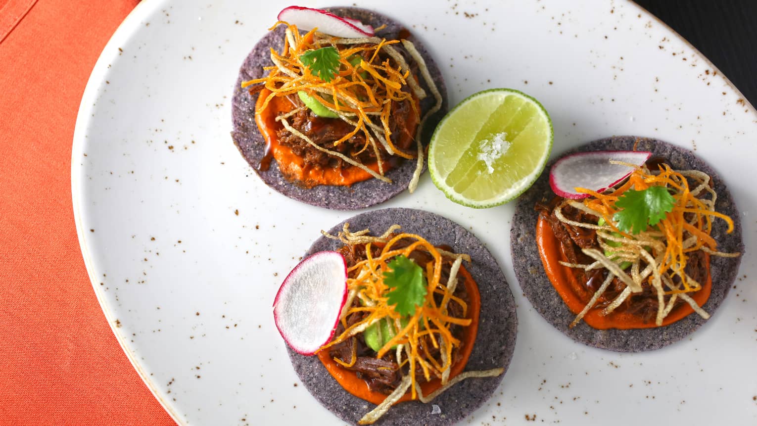 Three tacos with a lime wedge on a white plate.