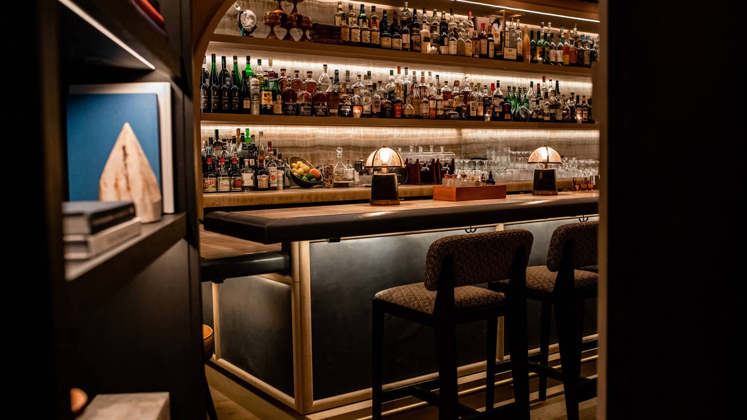 A bar with many bottles of liquor behind a bookcase.