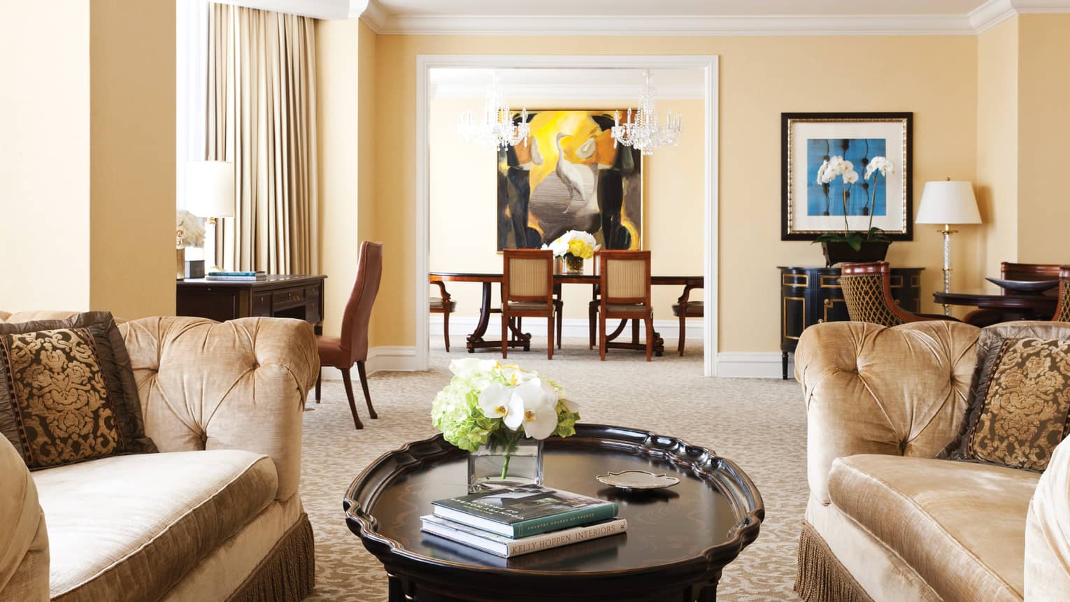 Presidential suite with large sofas around coffee table, books and flowers, dining room with crystal chandeliers