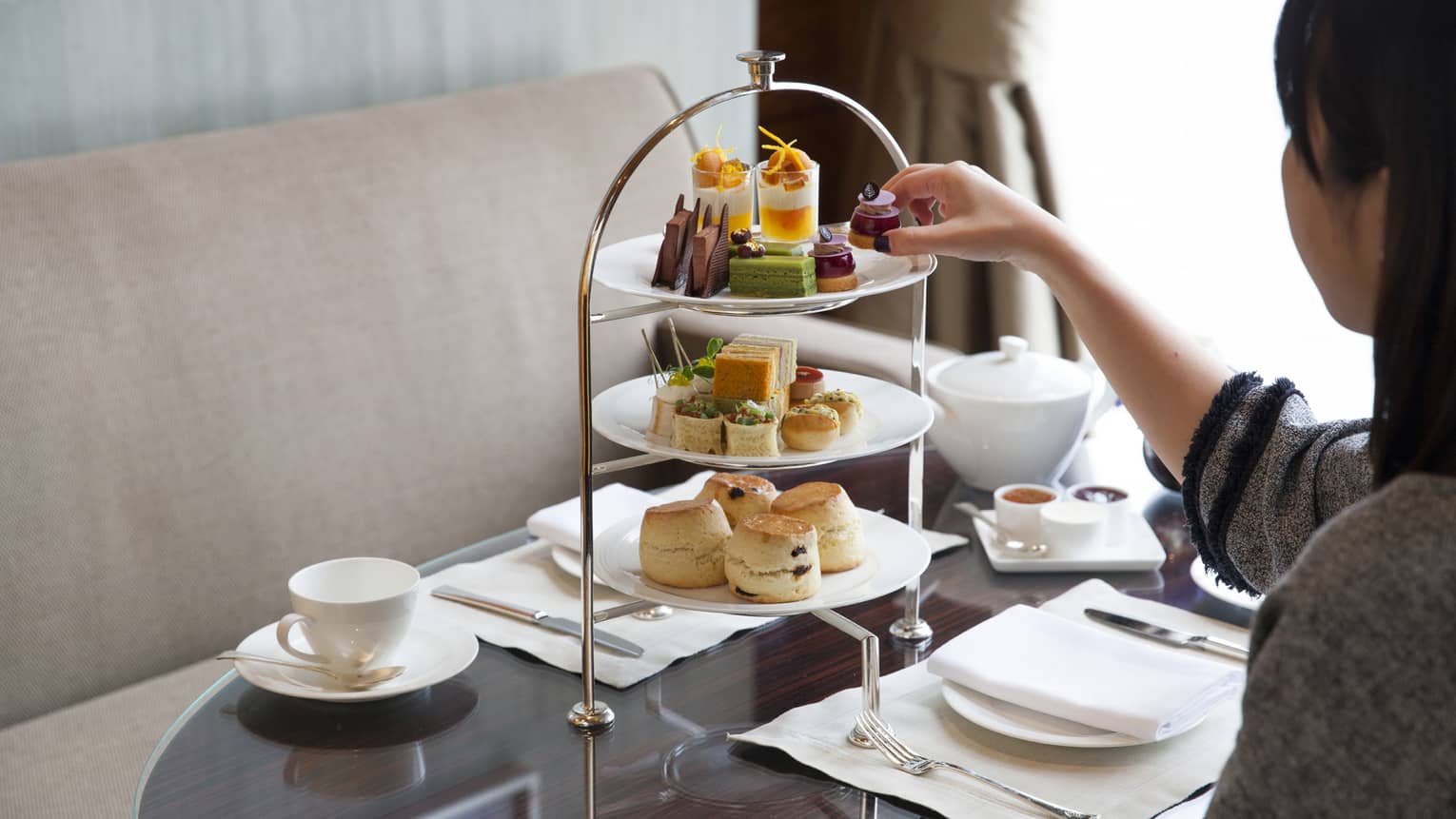 Woman reaches for small gourmet dessert on three-tiered tea service tray