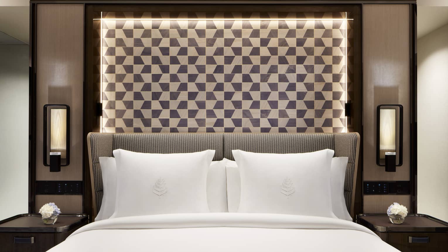 White bed with Four Seasons-embroidered pillows and checkered, illuminated headboard